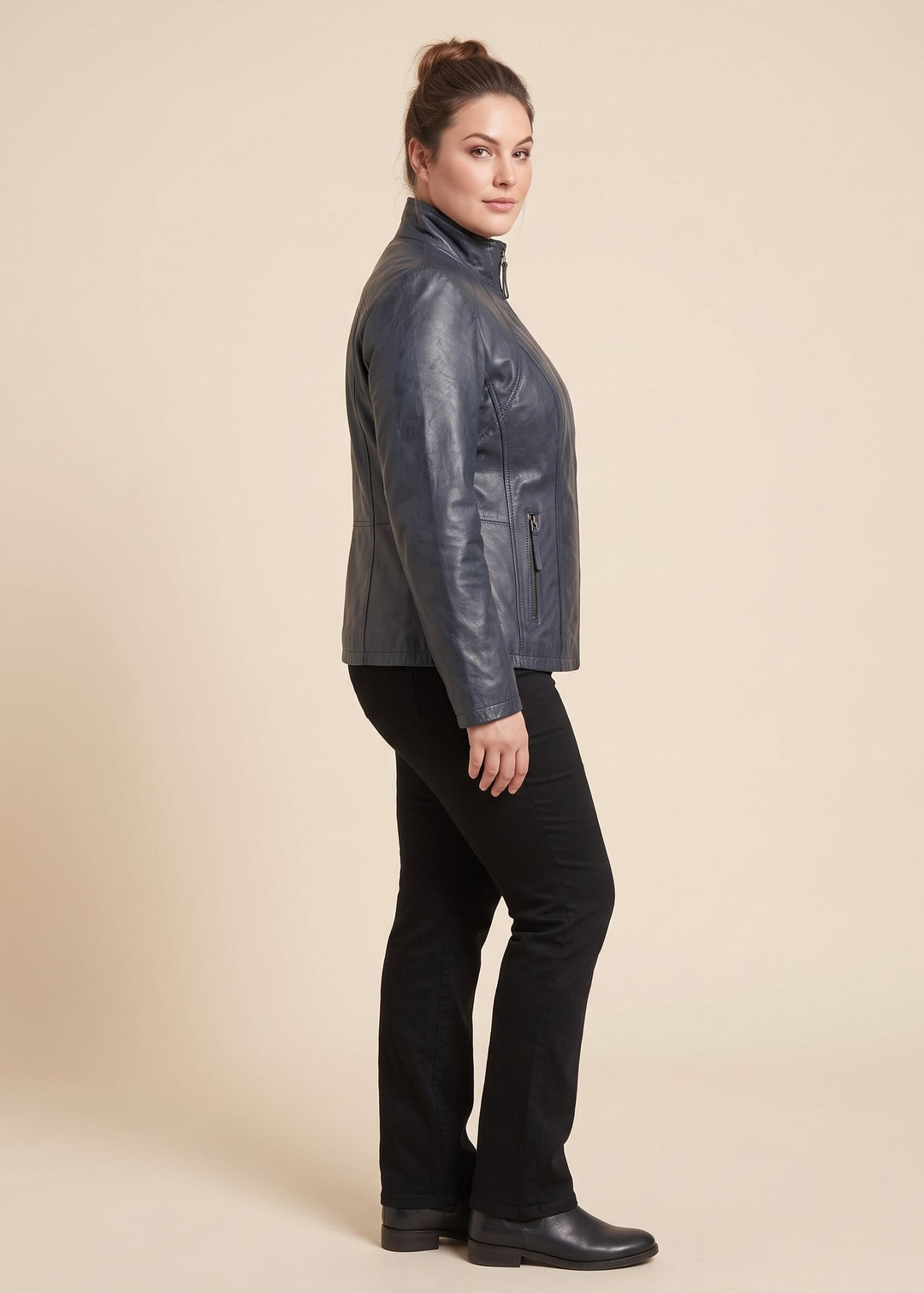 A woman modeling a navy real leather jacket, shown in profile against a solid beige studio background.