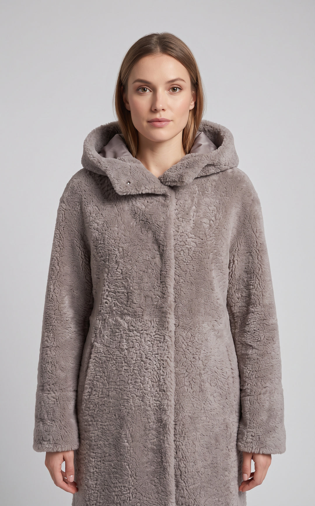 A woman wearing a plush, textured faux fur hooded coat in a taupe-gray color, photographed against a neutral light gray background.